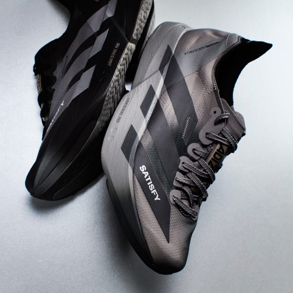 adidas ADIZERO ADIOS PRO 4 SATISFY in Core Black with Grey Five and Grey Three accents, showcasing minimalist technical racing apparel design